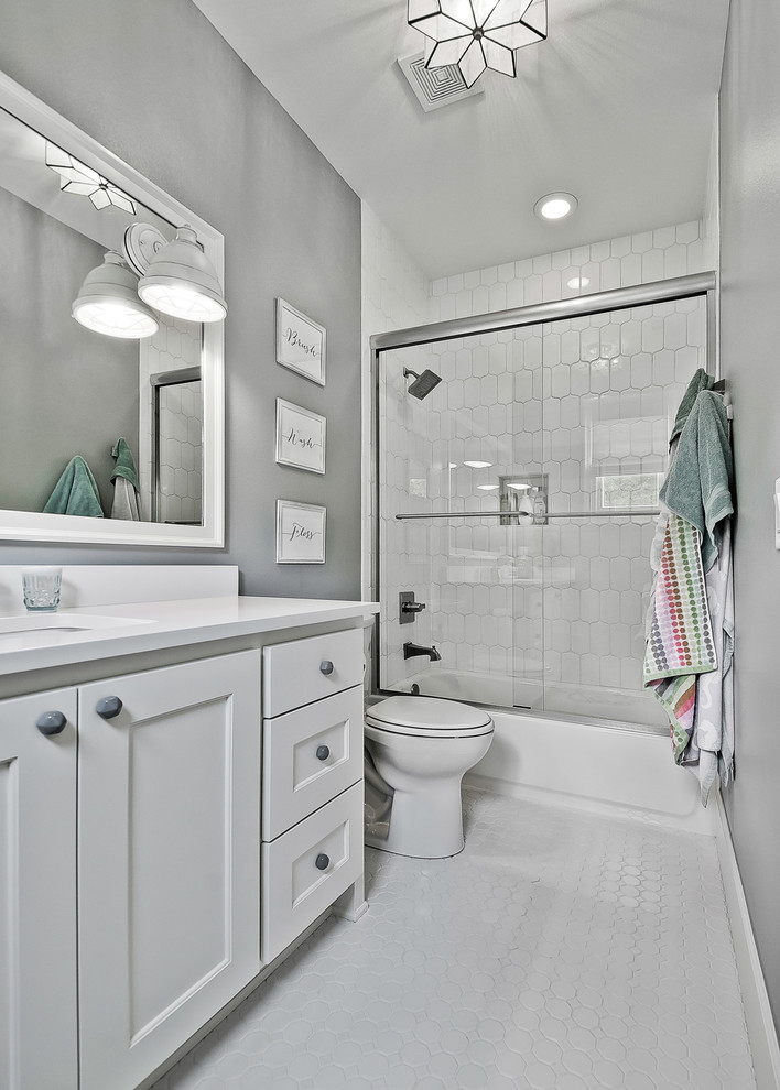 Large arts and crafts kids bathroom in Other with raised-panel cabinets, white cabinets, a shower/bathtub combo, a two-piece toilet, white tile, porcelain tile, grey walls, mosaic tile floors, an undermount sink, engineered quartz benchtops, white floor, a sliding shower screen and white benchtops.