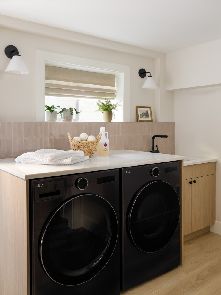 Mid-sized trendy l-shaped vinyl floor and beige floor dedicated laundry room photo in Seattle with an utility sink, flat-panel cabinets, light wood cabinets, quartz countertops, ceramic backsplash, white walls, a side-by-side washer/dryer and white countertops