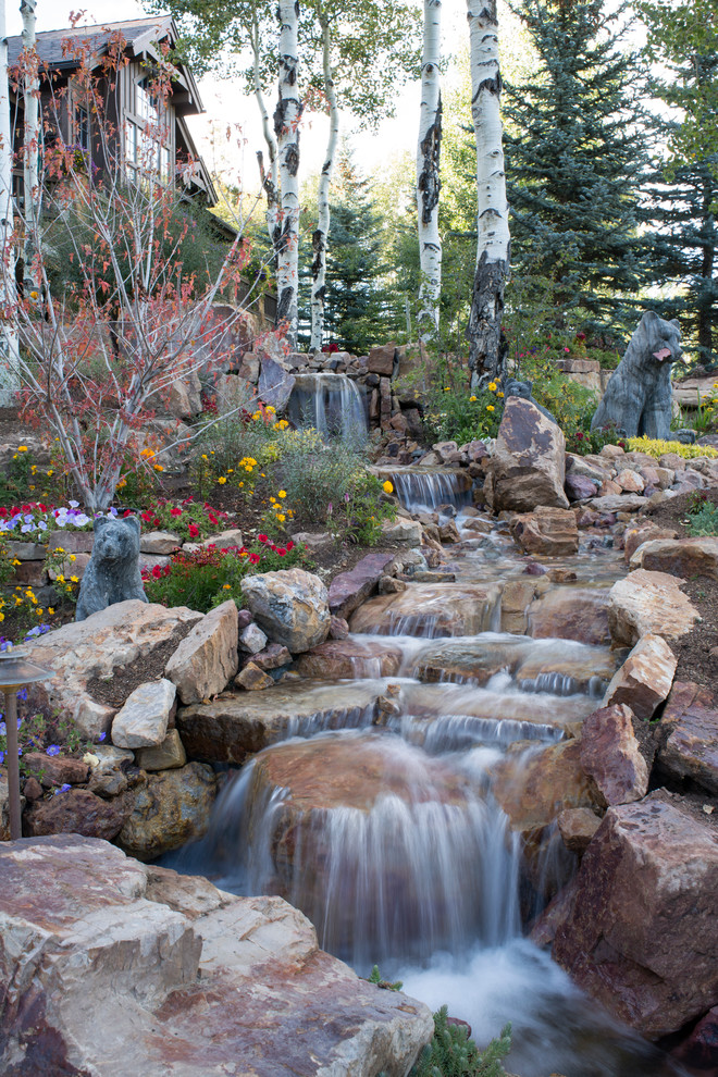 This is an example of an expansive country front yard partial sun garden for summer in Denver with natural stone pavers and with waterfall.