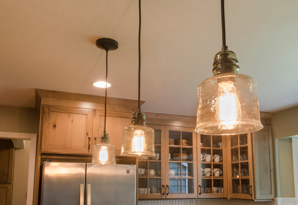 Mid-sized mountain style u-shaped medium tone wood floor enclosed kitchen photo with a farmhouse sink, shaker cabinets, medium tone wood cabinets, granite countertops, beige backsplash, ceramic backsplash, stainless steel appliances and an island