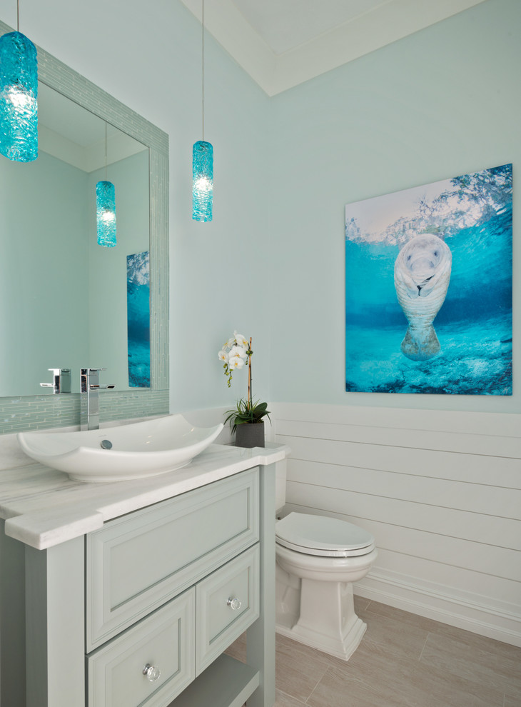 This is an example of a beach style powder room in Miami with recessed-panel cabinets, blue cabinets, blue walls, a vessel sink, beige floor and white benchtops.