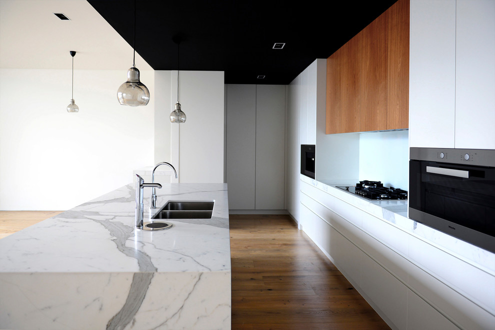 Inspiration for a mid-sized contemporary single-wall open plan kitchen in Melbourne with an undermount sink, white cabinets, marble benchtops, white splashback, marble splashback, stainless steel appliances, laminate floors, with island and beige floor.