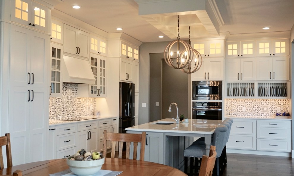 Kitchen pantry - large transitional l-shaped medium tone wood floor kitchen pantry idea in Cedar Rapids with an undermount sink, shaker cabinets, white cabinets, quartz countertops, multicolored backsplash, cement tile backsplash, stainless steel appliances and an island