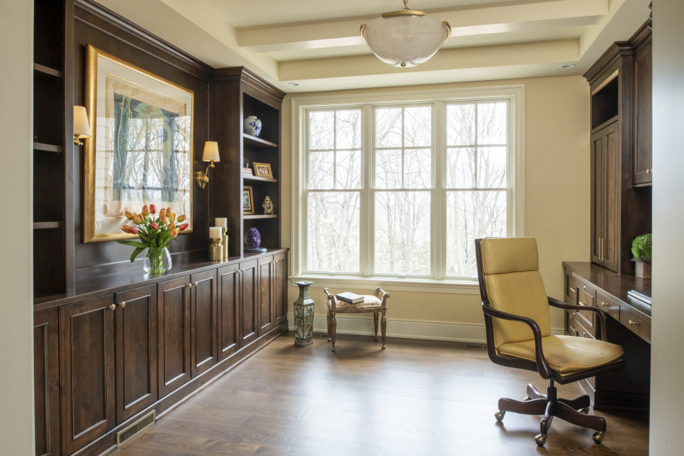 Foto de despacho tradicional renovado grande con paredes beige, suelo de madera oscura, escritorio empotrado y suelo marrón