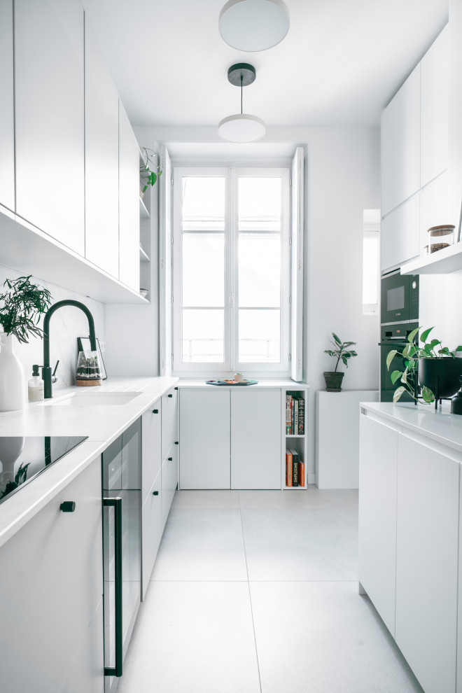 Idee per una cucina a L minimal con lavello sottopiano, ante lisce, ante bianche, paraspruzzi bianco, elettrodomestici neri, pavimento grigio e top bianco