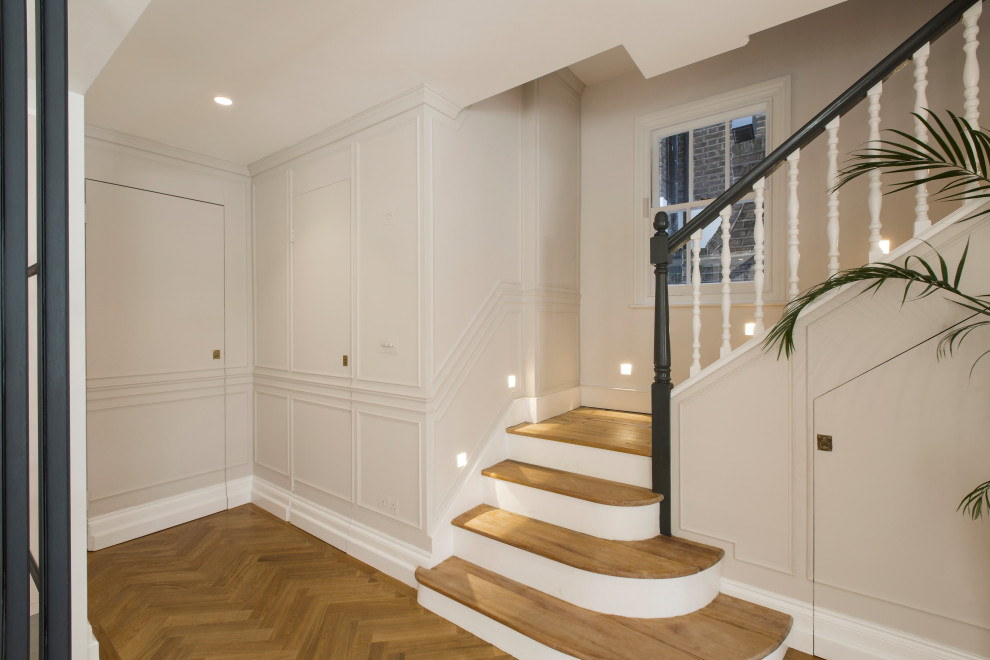 Large contemporary wood l-shaped staircase in London with painted wood risers, wood railing and panelled walls.