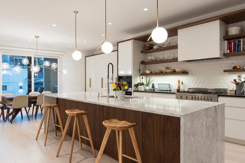 This is an example of a contemporary galley eat-in kitchen in Chicago with an undermount sink, flat-panel cabinets, white cabinets, white splashback, stainless steel appliances, light hardwood floors, with island and beige floor.