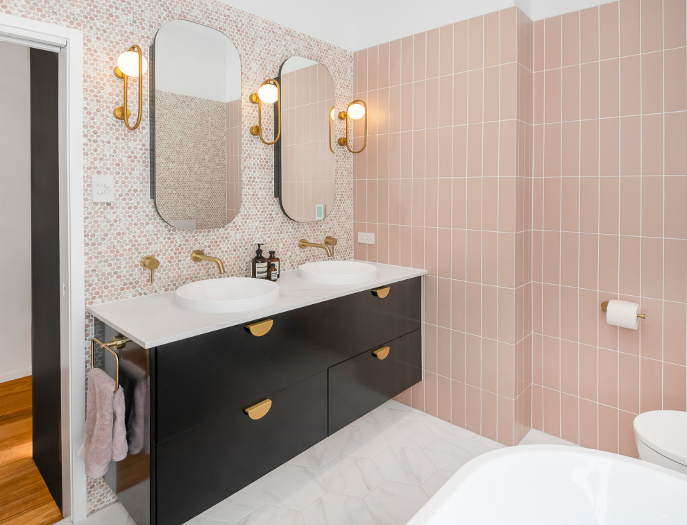 This is an example of a large contemporary master bathroom in Brisbane with furniture-like cabinets, black cabinets, a freestanding tub, an open shower, a wall-mount toilet, pink tile, mosaic tile, pink walls, ceramic floors, a vessel sink, marble benchtops, black floor, an open shower, white benchtops, a niche, a double vanity and a floating vanity.