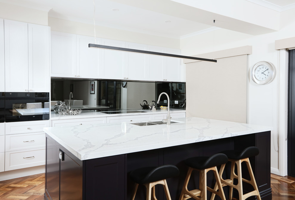 Inspiration for a mid-sized transitional galley open plan kitchen in Melbourne with an undermount sink, shaker cabinets, quartz benchtops, mirror splashback, black appliances, dark hardwood floors and with island.
