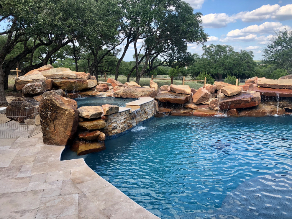 This is an example of an expansive country backyard custom-shaped natural pool in Austin with with privacy feature and decking.