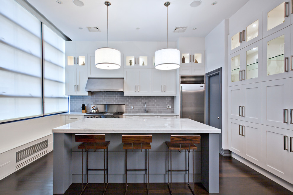 This is an example of a large transitional l-shaped open plan kitchen in New York with shaker cabinets, white cabinets, grey splashback, subway tile splashback, stainless steel appliances, dark hardwood floors, with island and a drop-in sink.