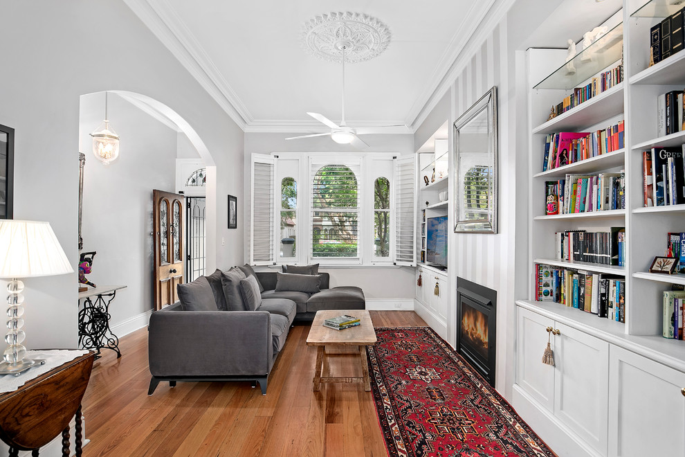 Inspiration for a traditional open concept family room in Sydney with white walls, medium hardwood floors, a standard fireplace, a built-in media wall and brown floor.