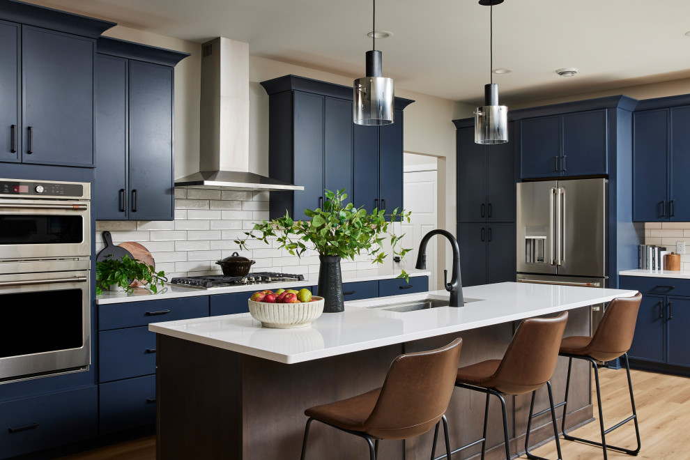 Large transitional l-shaped vinyl floor and beige floor eat-in kitchen photo in Minneapolis with an undermount sink, shaker cabinets, blue cabinets, quartz countertops, white backsplash, ceramic backsplash, stainless steel appliances, an island and white countertops