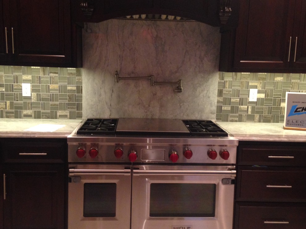 Inspiration for a timeless eat-in kitchen remodel with recessed-panel cabinets, dark wood cabinets, granite countertops, gray backsplash, glass tile backsplash, stainless steel appliances and an island