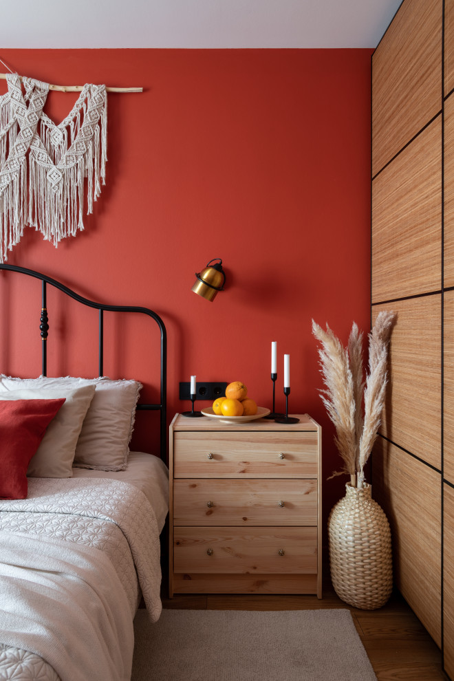 Aménagement d'une petite chambre parentale avec un mur rouge et un sol en bois brun.