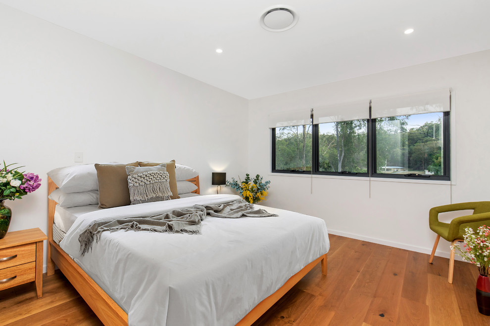 Photo of a transitional bedroom in Brisbane with white walls, medium hardwood floors and brown floor.