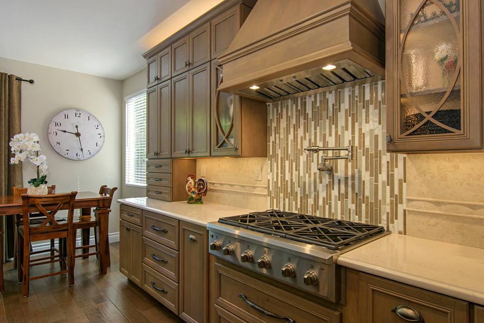 Inspiration for a large transitional l-shaped medium tone wood floor and brown floor open concept kitchen remodel in San Diego with a farmhouse sink, recessed-panel cabinets, medium tone wood cabinets, beige backsplash, paneled appliances, an island, quartz countertops and travertine backsplash
