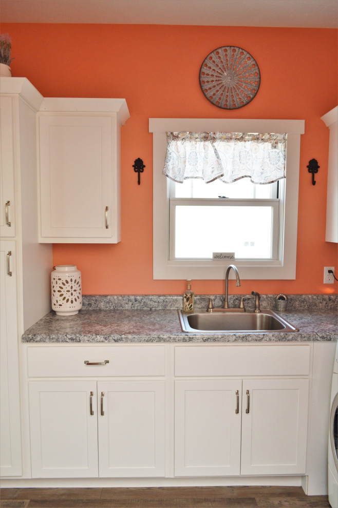 Inspiration for a mid-sized country l-shaped dedicated laundry room in Other with a drop-in sink, shaker cabinets, white cabinets, laminate benchtops, pink walls, laminate floors, a side-by-side washer and dryer, brown floor and grey benchtop.