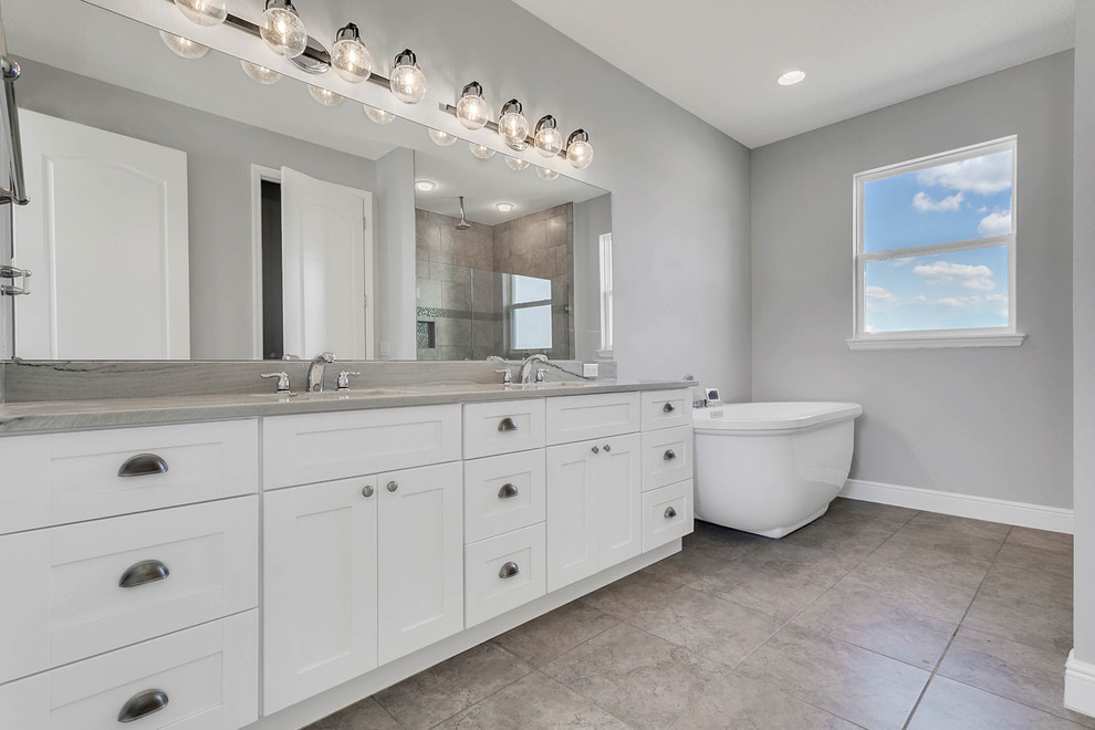 Photo of a large country master bathroom in Orlando with shaker cabinets, white cabinets, a freestanding tub, an open shower, a one-piece toilet, gray tile, mirror tile, grey walls, porcelain floors, an undermount sink, engineered quartz benchtops, grey floor, an open shower and grey benchtops.