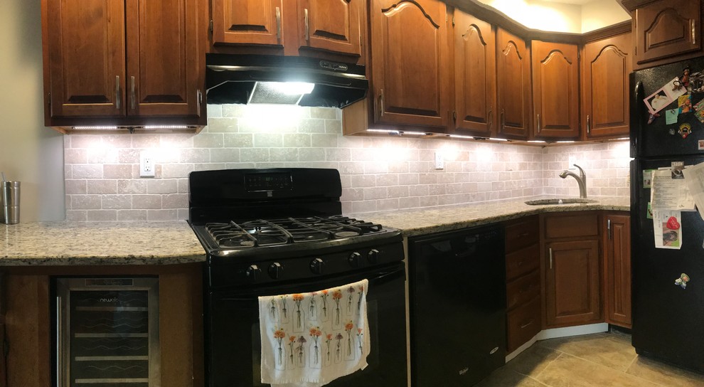 This is an example of a mid-sized galley separate kitchen in Philadelphia with an undermount sink, recessed-panel cabinets, brown cabinets, granite benchtops, beige splashback, travertine splashback, black appliances, ceramic floors, no island, green floor and beige benchtop.