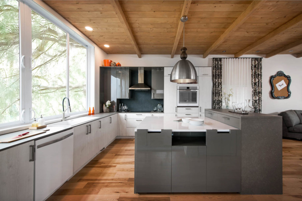 This is an example of a mid-sized contemporary l-shaped open plan kitchen in Montreal with an undermount sink, flat-panel cabinets, white cabinets, white splashback, stainless steel appliances, light hardwood floors, with island, matchstick tile splashback, quartz benchtops and beige floor.