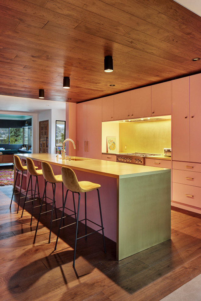Photo of a large mediterranean single-wall open plan kitchen in Los Angeles with an undermount sink, flat-panel cabinets, pink cabinets, yellow splashback, metal splashback, stainless steel appliances, dark hardwood floors, with island, yellow benchtop, wood and brown floor.