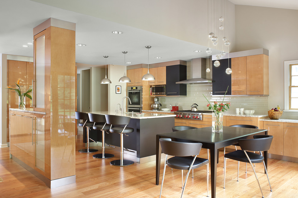 Photo of a contemporary galley eat-in kitchen in New York with flat-panel cabinets, light wood cabinets, granite benchtops, glass tile splashback, stainless steel appliances, light hardwood floors, with island and grey splashback.