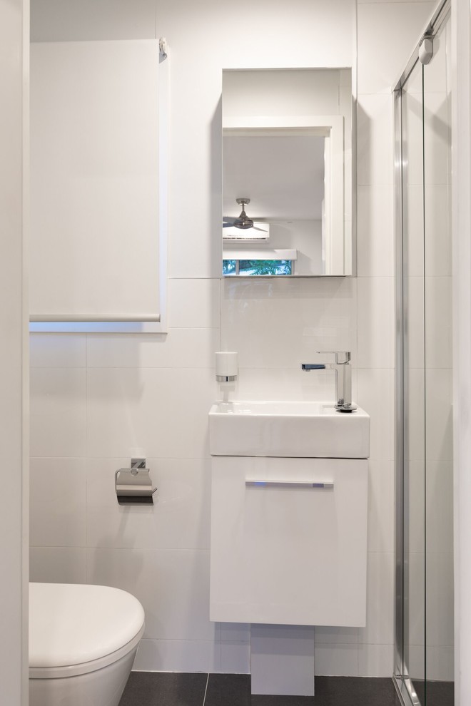 Inspiration for a small contemporary 3/4 bathroom in Brisbane with white walls, cement tiles, white benchtops, furniture-like cabinets, white cabinets, an alcove shower, white tile, ceramic tile, a drop-in sink, tile benchtops, black floor, a sliding shower screen and a wall-mount toilet.