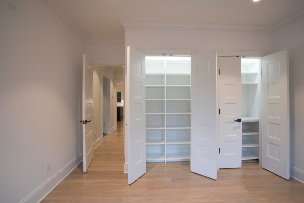 This is an example of a small transitional gender-neutral built-in wardrobe in New York with open cabinets, white cabinets, light hardwood floors and beige floor.