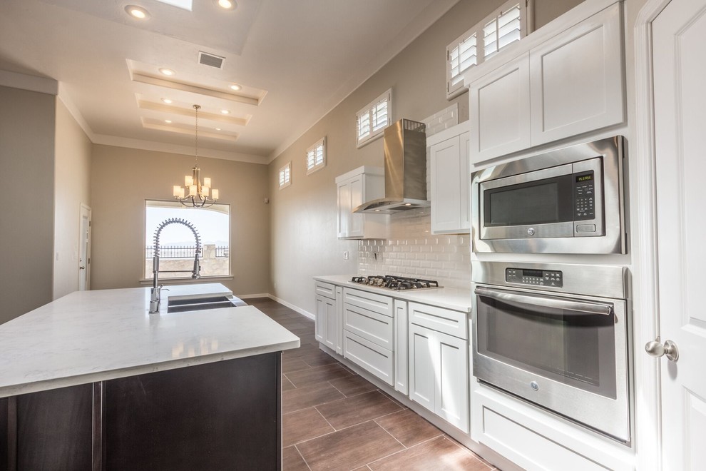 Eat-in kitchen - large transitional u-shaped ceramic tile eat-in kitchen idea in Austin with a farmhouse sink, flat-panel cabinets, white cabinets, quartzite countertops, gray backsplash, subway tile backsplash, stainless steel appliances and an island