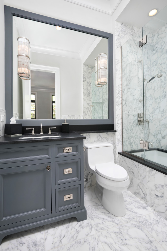 This is an example of a small transitional bathroom in Chicago with an undermount sink, recessed-panel cabinets, grey cabinets, granite benchtops, an undermount tub, a one-piece toilet, white tile, stone tile, grey walls and marble floors.