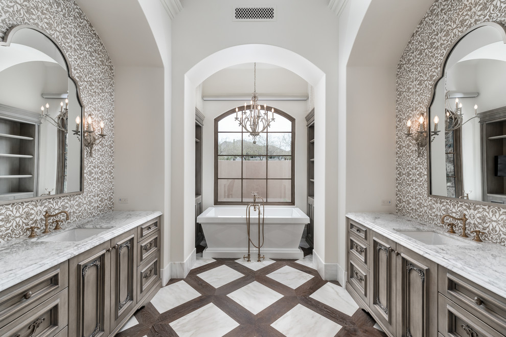 Photo of a mediterranean master bathroom in Phoenix with brown cabinets, a freestanding tub, brown tile, ceramic tile, dark hardwood floors, a drop-in sink, marble benchtops, brown floor, white benchtops, a double vanity, a built-in vanity and vaulted.