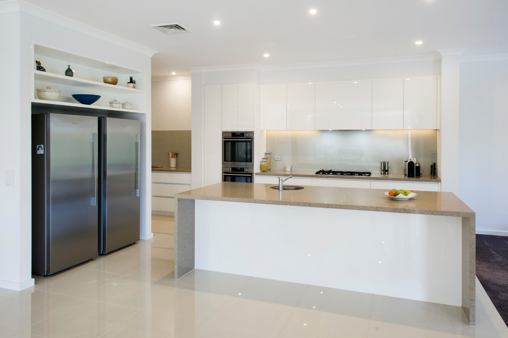 Design ideas for a modern galley open plan kitchen with an integrated sink, flat-panel cabinets, white cabinets, quartz benchtops, white splashback, glass sheet splashback, stainless steel appliances, ceramic floors, with island and white floor.