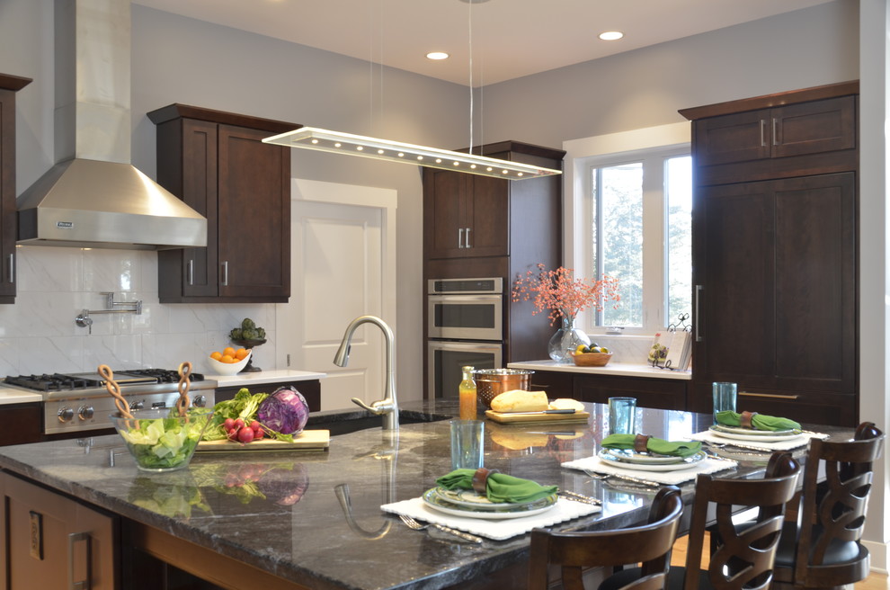 Open concept kitchen - large transitional u-shaped light wood floor open concept kitchen idea with an undermount sink, shaker cabinets, dark wood cabinets, quartz countertops, white backsplash, stainless steel appliances, an island and stone tile backsplash