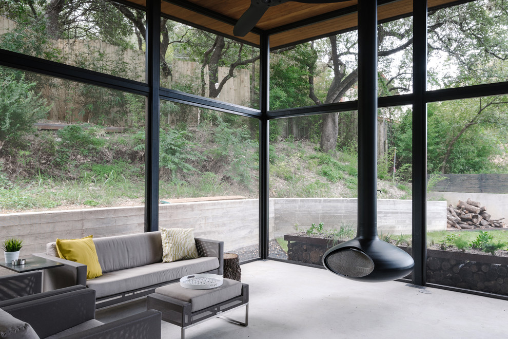 Photo of a modern sunroom in Austin with concrete floors, a hanging fireplace and a standard ceiling.