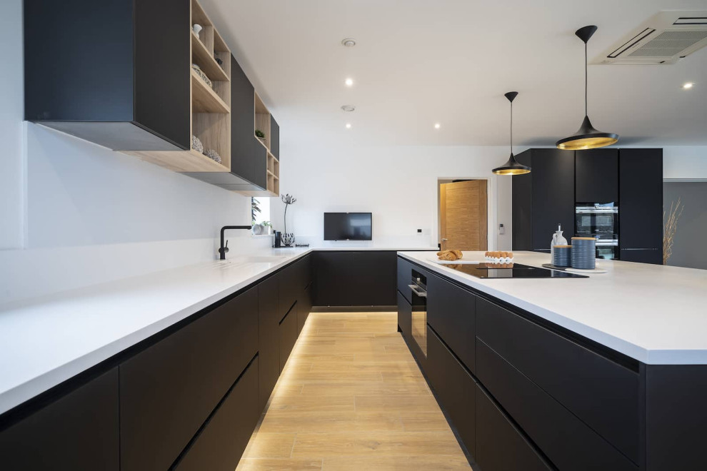 Design ideas for a large scandinavian l-shaped open plan kitchen in Oxfordshire with an integrated sink, flat-panel cabinets, black cabinets, quartzite benchtops, white splashback, black appliances, light hardwood floors, with island, brown floor and yellow benchtop.
