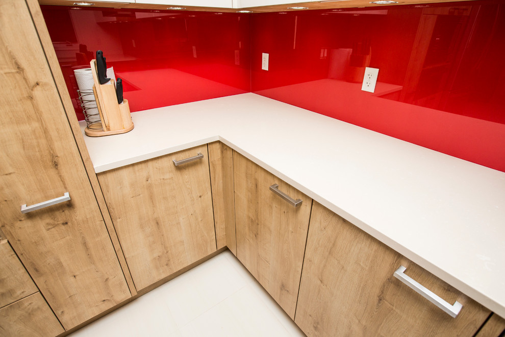 This is an example of a contemporary u-shaped eat-in kitchen in Toronto with an undermount sink, flat-panel cabinets, light wood cabinets, granite benchtops, red splashback, glass sheet splashback and stainless steel appliances.