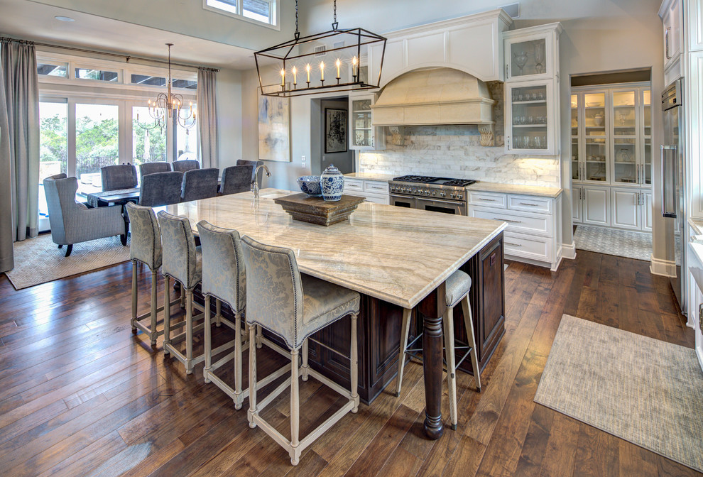 Inspiration for a large mediterranean l-shaped medium tone wood floor and brown floor open concept kitchen remodel in Austin with a farmhouse sink, recessed-panel cabinets, white cabinets, marble countertops, multicolored backsplash, subway tile backsplash, stainless steel appliances, an island and multicolored countertops
