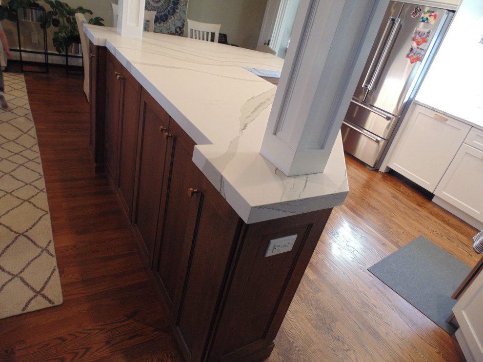 Example of a mid-sized transitional u-shaped medium tone wood floor and brown floor eat-in kitchen design with an undermount sink, recessed-panel cabinets, white cabinets, quartz countertops, white backsplash, stone slab backsplash, stainless steel appliances, no island and white countertops