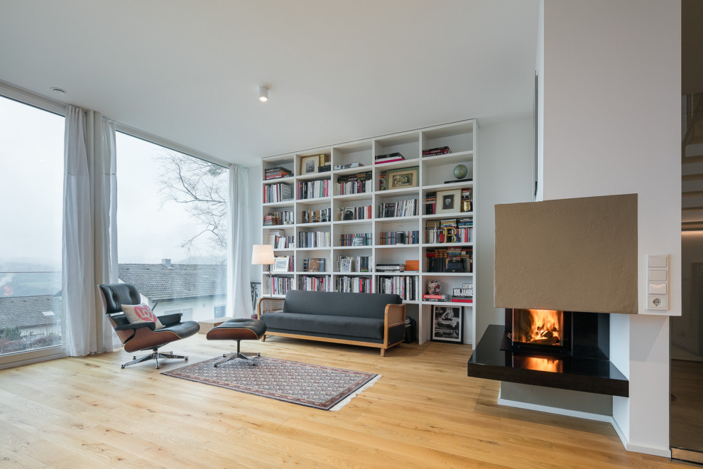 Große, Offene Moderne Bibliothek mit weißer Wandfarbe, hellem Holzboden, Kaminofen und braunem Boden in Stuttgart
