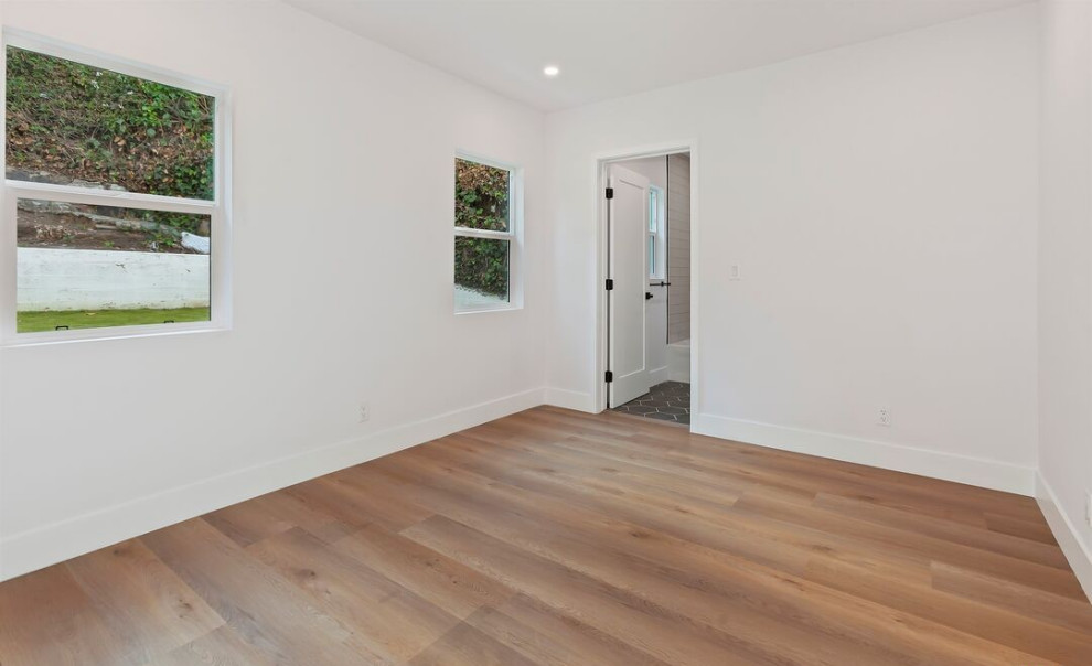 This is an example of a contemporary bedroom in Los Angeles with white walls, medium hardwood floors and brown floor.