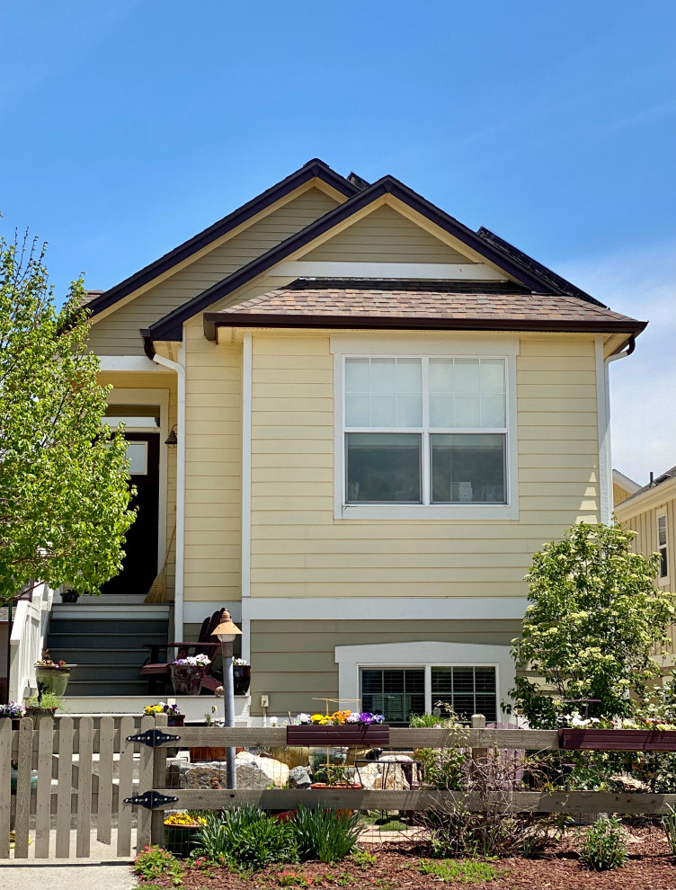 Пример оригинального дизайна: маленький, двухэтажный, желтый частный загородный дом в классическом стиле с облицовкой из ЦСП, двускатной крышей, крышей из гибкой черепицы и коричневой крышей для на участке и в саду