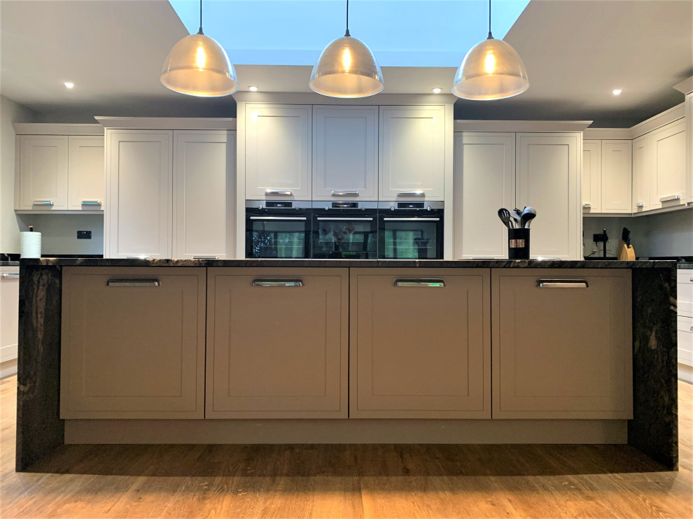 This is an example of a large traditional u-shaped open plan kitchen in Other with a double-bowl sink, shaker cabinets, medium wood cabinets, granite benchtops, black splashback, black appliances, vinyl floors, with island and black benchtop.