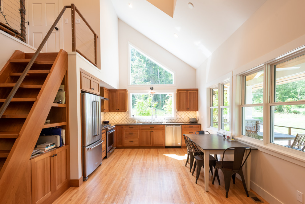 Small coastal l-shaped open plan kitchen in Seattle with a submerged sink, shaker cabinets, medium wood cabinets, engineered stone countertops, white splashback, ceramic splashback, stainless steel appliances, medium hardwood flooring, no island, brown floors, grey worktops and a vaulted ceiling.