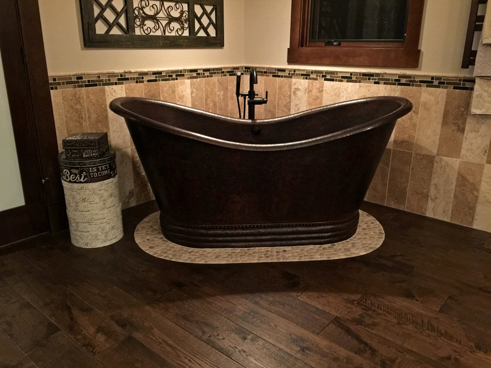 This is an example of a large country master bathroom in Calgary with shaker cabinets, distressed cabinets, a freestanding tub, a corner shower, a one-piece toilet, multi-coloured tile, stone tile, travertine floors, a vessel sink and granite benchtops.