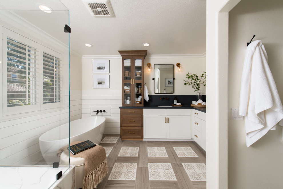 Country bathroom in Los Angeles with shaker cabinets, white cabinets, a freestanding tub, beige walls, an undermount sink, brown floor, black benchtops, a single vanity, a built-in vanity, planked wall panelling and decorative wall panelling.