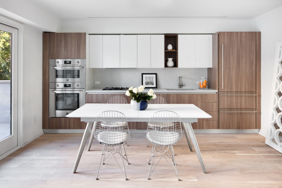 This is an example of a mid-sized contemporary eat-in kitchen in New York with a single-bowl sink, medium wood cabinets, granite benchtops, white splashback, granite splashback, stainless steel appliances, medium hardwood floors, beige floor and white benchtop.
