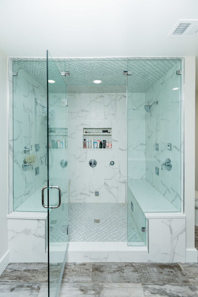 This is an example of a large transitional master bathroom in DC Metro with shaker cabinets, blue cabinets, an alcove tub, a corner shower, a two-piece toilet, white tile, marble, beige walls, plywood floors, an undermount sink, marble benchtops, brown floor, a hinged shower door and white benchtops.