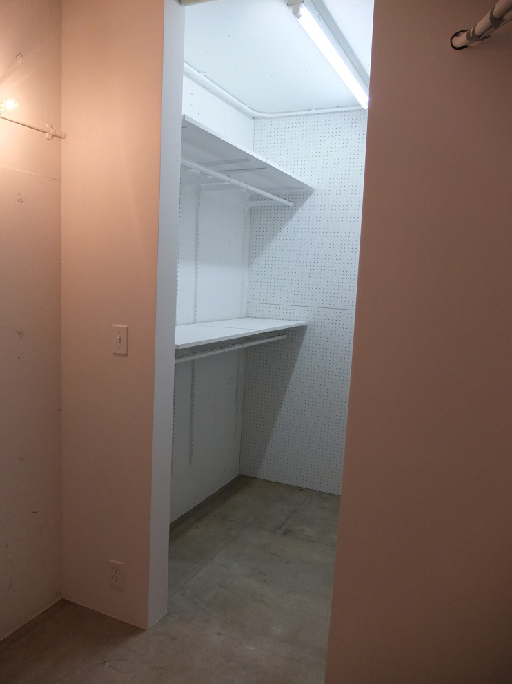 Idee per una piccola cabina armadio unisex minimalista con pavimento in cemento e travi a vista