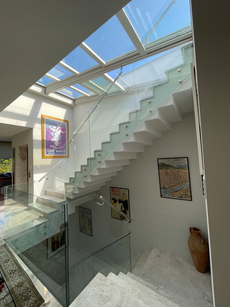 Стильный дизайн: большая п-образная лестница в стиле модернизм с мраморными ступенями, подступенками из мрамора и стеклянными перилами - последний тренд